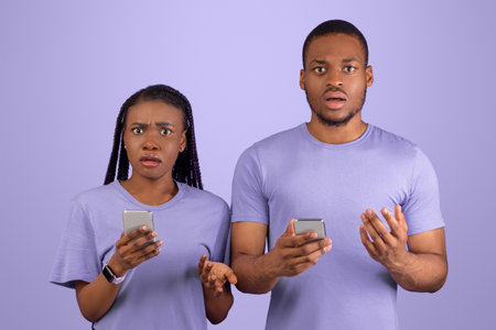 Confused millennial African American couple holding their mobile phones