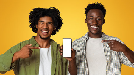 Mobile App. Two Cheerful Black Guys Pointing At Smartphone With Blank Screenの写真素材