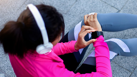 Black sporty girl with headset checking on fitness bracelet