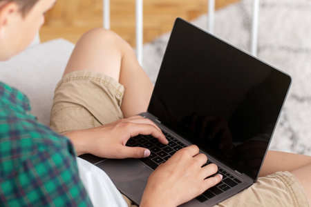 Teenager using laptop with blank screen, sitting at home