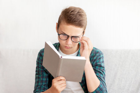 Schooler in glasses reading book at homeの写真素材