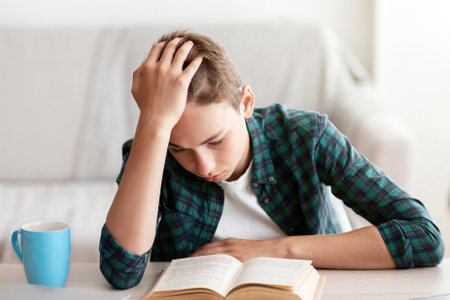 Bored teenager reading book, holding his headの写真素材