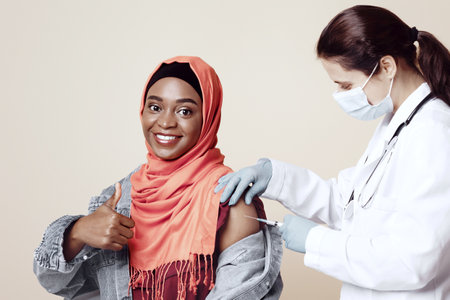 Muslim black woman in hijab getting vaccinated, showing thumb up