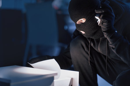 Masked thief holding and reading confidential documentsの写真素材