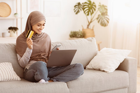 Online Shopping. Muslim woman using smartphone, laptop and credit card at homeの写真素材