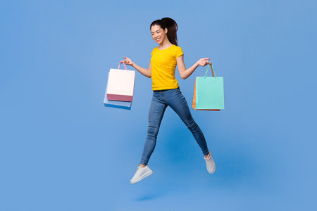 Happy Shopping. Joyful Asian Girl Jumping In Air With Lots Shopper Bags