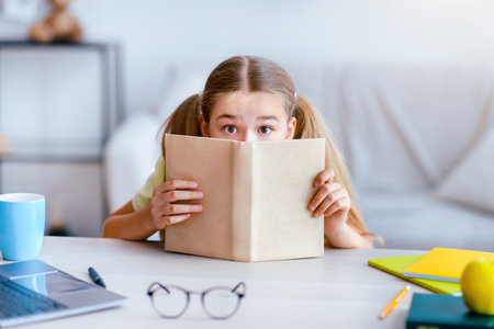 Scared girl with wide open eyes hiding behind a bookの写真素材