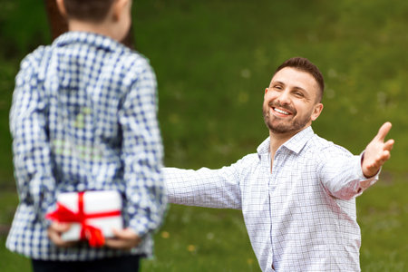 Fathers Day celebration. Little kid hiding gift for his dad behind his back on picnic in parkの写真素材