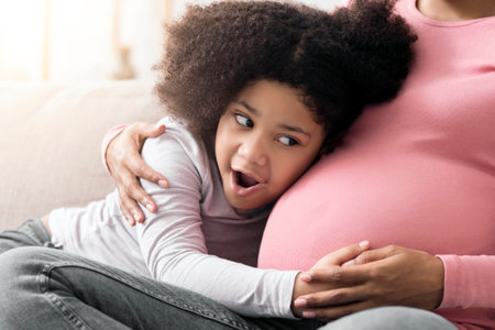 Excited little girl touching and listening to her pregnant mothers bellyの写真素材