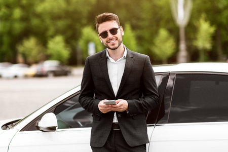 Happy corporate manager using cellphone near his auto at city centerの写真素材