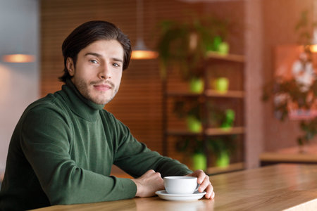 Young handsome man sitting alone at cafe, drinking coffeeの写真素材