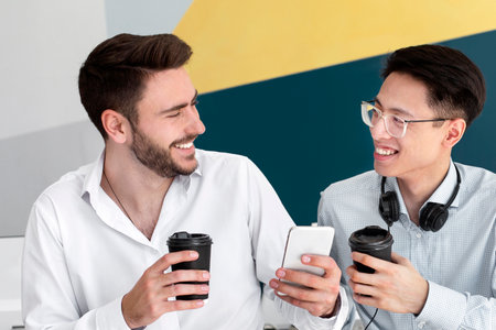 Male helpdesk agents browsing internet on smartphone during coffee break at modern call center, copy spaceの写真素材
