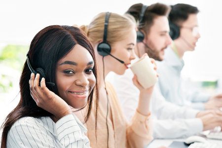 Group of call centre representatives with headsets working on computers at light open space office, space for textの写真素材