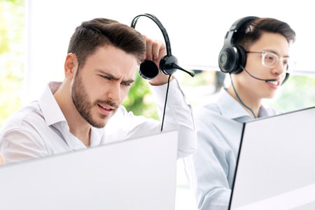 Stressed call center operator listening to clients complaint at contemporary officeの写真素材