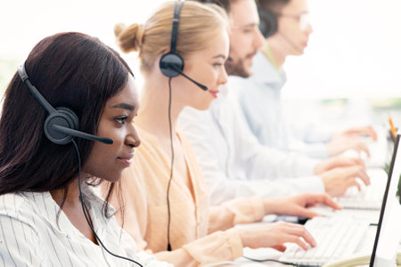 Focused call centre operators with headphones working with computers at open space office, blank spaceの写真素材