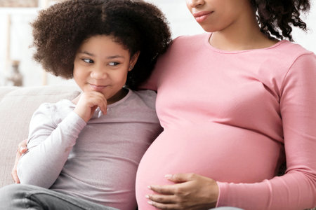 Excited Little Afro Girl Looking At Pregnant Moms Tummy With Curiosityの写真素材