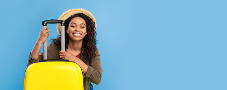Smiling young African American lady sitting behind bright yellow suitcase, going on summer vacation, having abroad tripの写真素材
