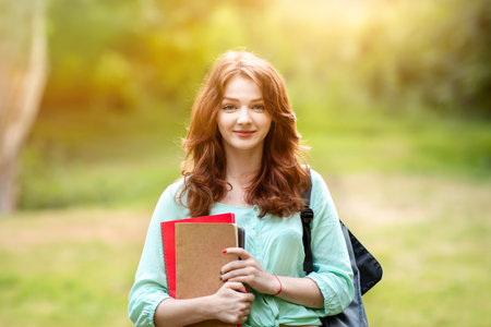 Attractive redhead student girl with backpack and workbooks posing at campus yardの写真素材
