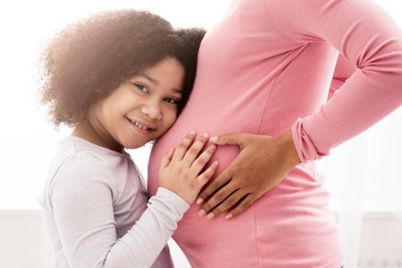 Happy Expectation. Cute Little Afro Girl Cuddling Mothers Pregnant Bellyの写真素材