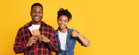 Happy African Tourists Holding Tickets Gesturing Thumbs-Up On Yellow Backgroundの写真素材
