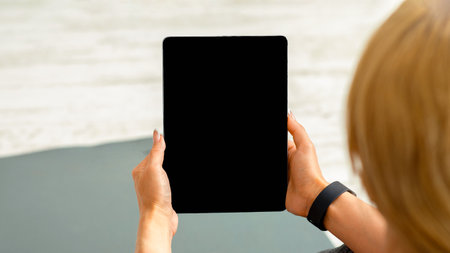 Home workout with devices. Adult woman with fitness tracker and tablet sits on matの写真素材