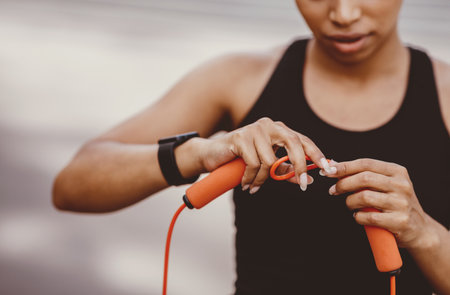 Adjustment of sports equipment. Girl in sportswear with fitness tracker adjusts skipping rope for workoutの写真素材