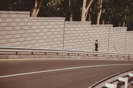 Female runner sprinting on street. African american girl in sportswear fast runs along trackの写真素材