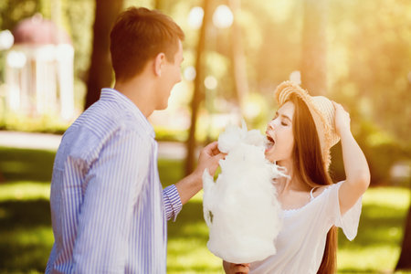 Romantic times together. Happy millennial couple eating candy floss together outdoors in summerの写真素材