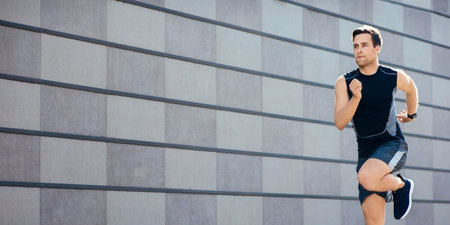 Fast running on training in city. Athletic man in sportswear with fitness tracker runs and jumps