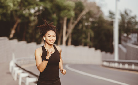Girl runs in summer at city. Woman with fitness tracker runs along trackの写真素材