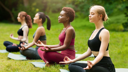 Concentrated multinational women deep in meditation during outdoor yoga class at park, empty spaceの写真素材