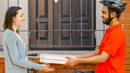 Pizza delivery service. Smiling courier in helmet with bicycle gives box for client at house