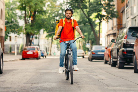Express delivery service. Cyclist with helmet and yellow backpack rides on roadの写真素材