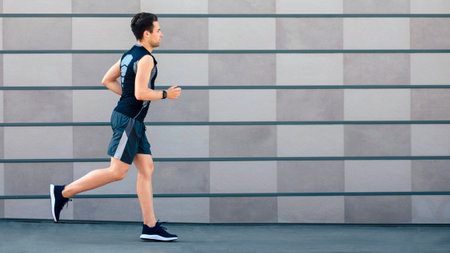 Running in morning in city. Guy with fitness tracker on hand runs at path
