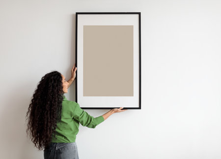 Happy Woman Hanging Empty Poster In Frame On Wall Indoorsの写真素材