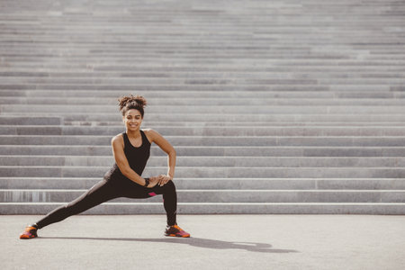 Young woman and active workout on street. Girl in sportswear with fitness tracker does exercises on stairsの写真素材