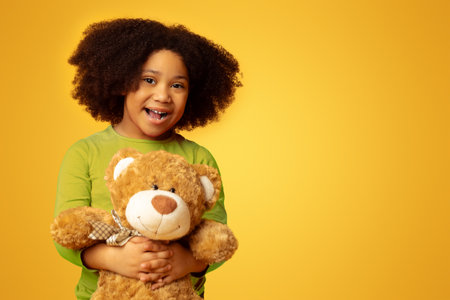 Happy little black girl with big teddy bear over yellow backgroundの写真素材