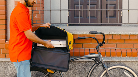 Delivery home and office. Young delivery man takes out pizza from big yellow backpack on bicycle