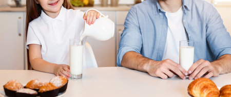 Father Looking At Daughter Pouring Milk In Glass In Kitchenの写真素材