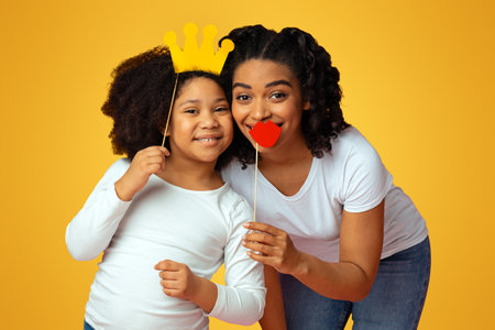 Happy black mother and her daughter posing with paper party accessoriesの写真素材
