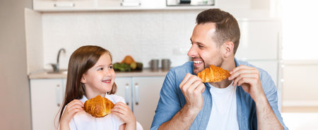 Father And Daughter Having Croissants For Breakfast Sitting In Kitchenの写真素材