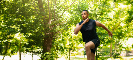 Handsome millennial sprinter running on track at beautiful park, copy space