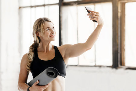 Beautiful woman in sportswear with mat in her hands make photo for blog