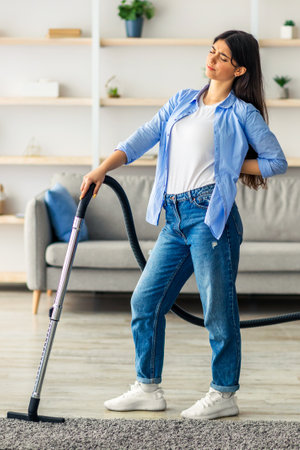Young woman cleaning the living room while stretching her back at homeの写真素材