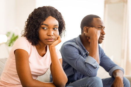 Frustrated african man and woman sitting on couch at homeの写真素材