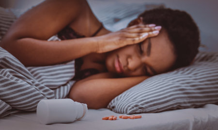 Pills sprinkled from jar on bed, african american girl cannot fall asleepの写真素材