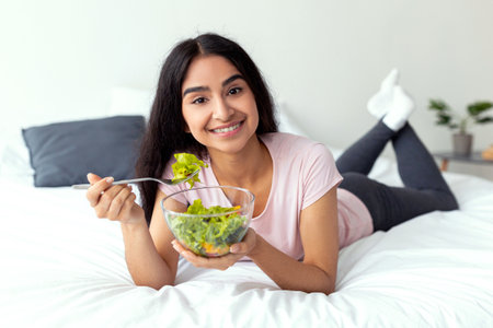 Young Indian woman enjoying a healthy salad while relaxing at homeの写真素材