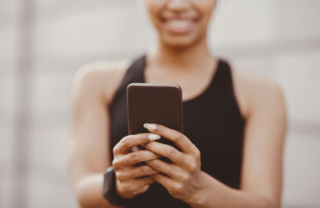 Sports and social networks. Smiling woman in sportswear with fitness tracker typing at smartphoneの写真素材