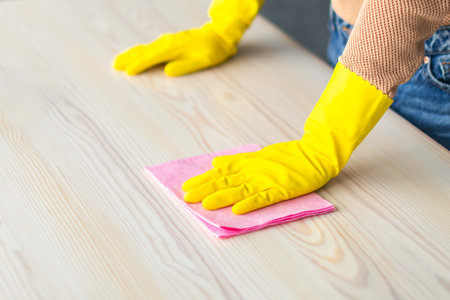 Young woman cleaning a wooden table with a cloth at home during daylight hoursの写真素材