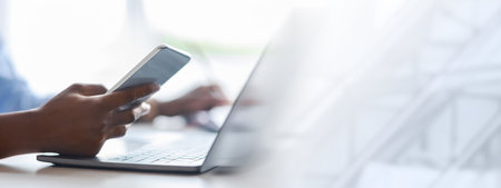 Unrecognizable black woman using smartphone and working on laptop in office, closeupの写真素材